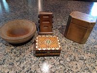 Four vintage wooden items on granite countertop: wooden bowl, tea caddy, carved box, and carved holder