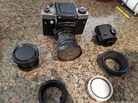 Camera body with Helios lens, prism finder, lens hood, caps and filter on countertop