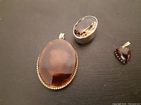 Photo showing the three jewelry items together including a large brown oval item, a silver brooch with faceted smoky quartz stone, and a small deep red pendant