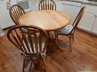 Wide shot showing the vintage round oak dining table with four matching chairs placed around it in a kitchen setting.