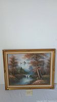 Frontal photo of the framed oil painting depicting a landscape with a stream and trees.