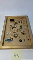 Full view of costume jewelry lot displayed on a wooden tray with various brooches, pins, necklaces, ring, wristwatch, and earrings.