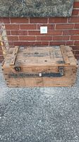 Rectangular wooden storage crate with metal latch, hinge, and handle, showing worn wooden surface with markings "944 SIGNALS" on the lid and sides.