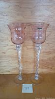 Two tall, hand blown stem glasses with twisted stems in front of wood background.
