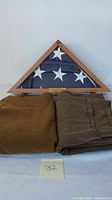 Triangular wooden display case containing folded U.S. flag and two folded blankets beneath.