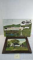 Photo of two primitive style oil paintings on board by Robert L. Merriam, showing landscapes with houses, grouped together for lot documentation.
