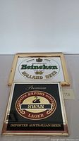 Full view of two vintage beer bar mirrors with wooden frames showing wear: Heineken and Swan Lager.