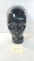 Front view of vintage black glass mannequin head on white background with identification card showing number 45.