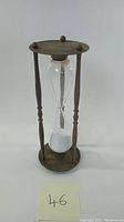Front view of vintage brass hourglass sand timer standing upright showing entire piece.