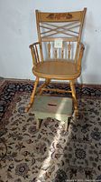 Full view of the hand-painted vintage child's rocker chair and green foot stool on a patterned rug.