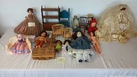 Front overview showing the assortment of vintage dolls and furniture spread on a white surface. Eleven dolls visible including bisque, porcelain, and stuffed dolls with a variety of vintage wooden and wicker furniture pieces.