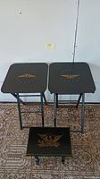 Two black lacquer folding tables and one matching stool with gold eagle stencils seen from front and above on carpet