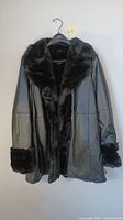 Front view of the vintage black leather coat with large furry collar and fur cuffs shown on hanger.