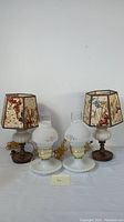 Photo of two pairs of vintage milk glass table lamps, shorter pair in front and taller pair behind with decorative floral fabric shades.