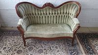 Full front view of light green velvet tufted loveseat with carved wooden frame