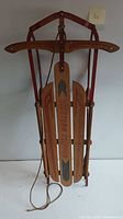 Full front view of vintage Western Clipper wooden snow sled folded upright showing red frame and wood slats with branding and decorative painting.