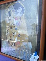 Framed poster of Gustav Klimt's The Kiss with visible folds, captured at an angle showing details of the artwork and wooden frame.