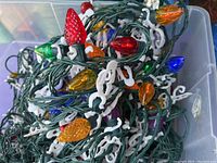 Close-up of colorful Christmas light string with green wiring and white hanging clips, bulbs in red, green, orange, blue, purple colors, with textured pinecone-shaped bulbs