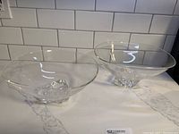 Pair of clear Steuben glass bowls displayed side by side on a marble surface with white subway tile background.