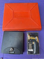 Red Weller soldering kit case, black Sentry money box, and Etekcity Lasergrip D80 infrared thermometer in packaging displayed on purple cloth.