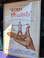 Full view of the framed Tom Thumb musical movie poster showing the title, illustration of a tiny man on a hand, and various text elements.
