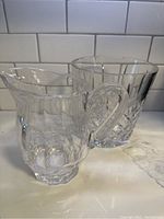 Ice bucket and pitcher displayed side by side on a marble surface against a white subway tile backsplash, showing crystal clarity and cut pattern