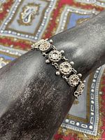 Silver bracelet on a black display stand, showing the full bracelet design with linked circular motifs and small ball decorations.