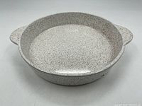 Front view of round speckled Blue Mountain Pottery stoneware dish with two handles, showing texture and glaze.