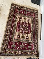 Full view of the rug showing the central red medallion with geometric designs on ivory background and bordered with multiple motif bands.