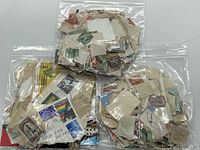 Two plastic bags containing assorted vintage used postage stamps affixed to paper pieces, various colors and postmark cancellations visible.