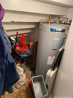 Photo of corner with orange bottle dryer, water heater, folding tables, plastic containers, and small metal bin