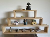 Full view of lot displayed on tiered wooden shelf showing all items including bell, pin, miniature buildings, fish figurine, and geodes laid out.