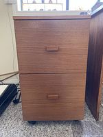 Front view showing two drawers with wooden handles and teak finish on a carpeted floor.