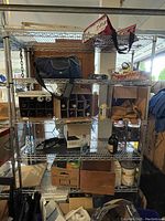 Full view of metal shelving unit with items including bags, wine racks, cardboard boxes, paint cans, and bottle on shelves.