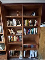 Photo showing two tall wooden bookshelves filled with books and some decorative objects, placed side by side.