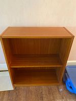 Front view of small teak shelving unit showing two shelves and wood grain.