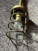 Close-up of the light bulb and surrounding brass protective cage on the vintage hanging fixture.