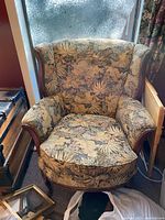 Front view of vintage upholstered armchair showing floral leaf pattern fabric and carved wooden arms.