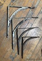 Four metal brackets laid out on wooden floor showing various sizes and wear condition.