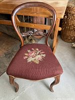Front view of antique balloon back chair showing needlepoint floral upholstered seat and wood frame with cabriole legs.