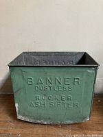 Front view of green metal antique ash sifter, showing embossed branding and dustless rocker ash sifter text.
