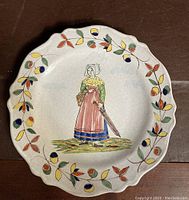 Front view of scalloped edge earthenware plate with central figure of a woman and colorful floral border.