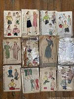 Lot of 12 vintage sewing patterns displayed showing front illustrated envelopes with female and male fashion designs.