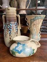 Three vintage English pottery vessels: two tall vases and one low pitcher, displaying painted and embossed flower and foliage decorations.