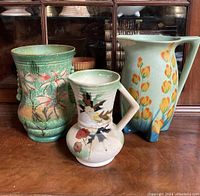 Photo showing entire lot of three vintage English pottery pieces: green vase, cream floral pitcher, and tall floral pitcher.