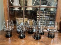 Seven vintage smoked glass drinking glasses arranged on a wooden surface, front view showing the entire set.