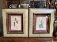 Pair of framed vintage male and female color plates shown together on table.