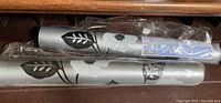 Two rolls of wallpaper rolled and wrapped in plastic showing silver base and black floral design
