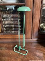 Front view of the green metal hat holder stand showing the dome-shaped top, pull cord, and base.