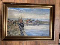 Framed original painting of boats docked beside a stone quay, with houses and other boats in the background under a cloudy sky.